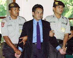 Ali Imron is escorted by police officers as he arrives at a courtroom in Denpasar