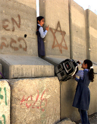 Two schoolgirls slip through a wall separating Palestinian and Israeli territories during a demonstration against the building of the wall in Jerusalem