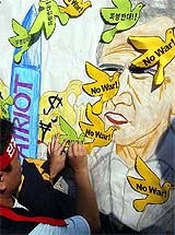 A South Korean protester attaches a paper dove with slogan, meaning "No War and No dispatch", on a painting of US President George W. Bush at a rally to oppose the dispatch of South Korean Army to Iraq
