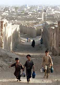 Afghan boys carry water as they walk through destroyed houses