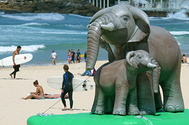 Inflatable African elephants, a mother and calf, tower over beach goers