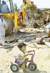 A child goes about her business as a bulldozer razes unauthorised structures