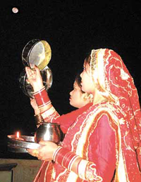 Women in bridal finery looking at the moon through a sieve to break their fast on the occasion of Karva Chauth.