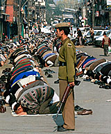 A policeman stands guard as Kashmiri Muslims offer prayers on the second day of the Islamic holy month of Ramzan in Srinagar