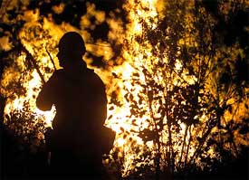A silhouetted firefighter walks past approaching flames on the east side of Descanso,