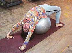 A woman uses a Swiss ball to perform exercise to strengthen her back