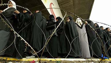 Iraqi women gather behind razor wires to collect compensation payments for war widows in the northern Iraqi city of Mosul