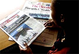 A woman looks at two daily newspapers, declaring Zimbabwe's withdrawal from the Commonwealth