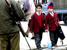 Two school children walk past a soldier as he patrols a street in Srinagar in this December 12, 2003 file photo
