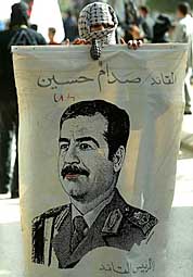 A masked Palestinian holds up a banner with the picture of Saddam Hussein during a protest over his capture by the US forces in the Northern Iraqi city of Tikrit on Monday