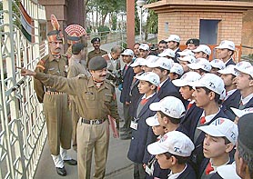 A BSF official points towards the Pakistan side at Wagah joint checkpost along with children from Jammu and Kashmir
