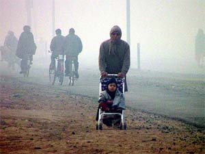 A man takes a kid for a ride on a perambulator amid thick fog in Bathinda 