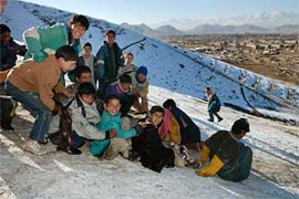 Afghan boys slide down the slope of a hill after this season's first snowfall in Kabul on Tuesday