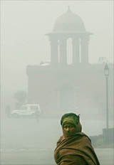 A man wearing a woollen scarf walks on a cold and foggy morning in New Delhi