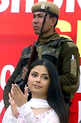 Bollywood actress Samreen claps as a policeman stands guard during the launch of her film Sheen, in Jammu on Saturday