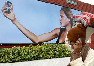 A man talks on a mobile phone near a hoarding promoting mobile telephones in New Delhi.