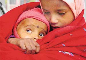 An infant huddles in a shawl with her six-year-old sibling to ward off the chill
