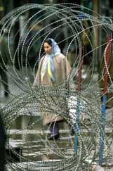 A woman walks behind a fence of a security installation in Srinagar