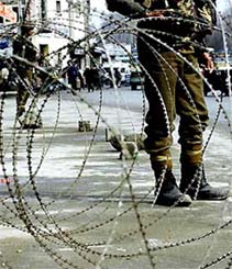 BSF soldiers stand guard next to a barbed-wire security barricade on a street in Srinagar
