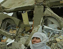 A Palestinian woman sits in front of the rubble of her house