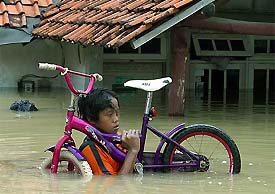 A boy carries his bicycle through a flooded neighbourhood of Jakarta 