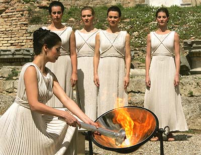 Greek actress Thalia Prokopiou, dressed in a white robe as the high-priestess, lights a torch using the sun's rays in a parabolic mirror during a dress rehearsal of the traditional Olympic lighting ceremony in ancient Olympia
