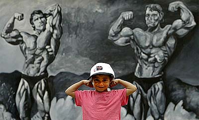 Four-year-old Arnold Mehdi, who is named along with his father's gymnasium after actor and California Governor Arnold Schwarzenegger, poses in front of a mural in Baghdad 