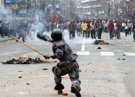 A policeman retaliates as demonstrators throw stones