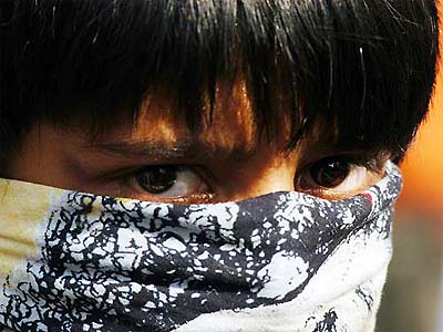 A young boy covers his face to hide his identity while throwing stones at the police in Kathmandu 
