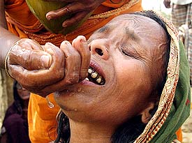 A tornado survivor uses her palms to feed coconut water to another grieving survivor at a devastated village in northern Bangladesh