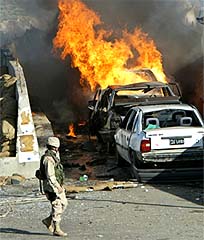 A US soldier walks past a burning car following an explosion outside the headquarters of the US-led coalition in Baghdad 