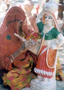 A woman paints a statue on the roadside unmindful of the blazing sun