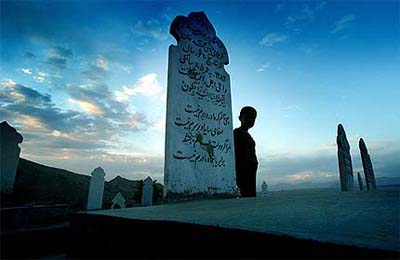 A boy stands next to the grave of a woman named Habiba who died at the age of 85, at a cemetery in Kabul