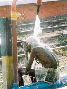 An old man makes good use of the pressure shower at the railway station installed for cleaning the tracks.