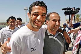 Iraqi footballer Hassan Turkey smiles as he walks with an official on their arrival in Baghdad on Tuesday