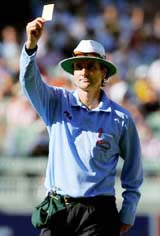 New Zealand umpire Billy Bowden shows a yellow card to World XI's Shane Warne for walking off the ground while batting