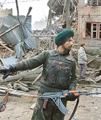 An Army jawan stands guard outside a damaged house where three militants were killed after a 24-hour gun battle at Batpora