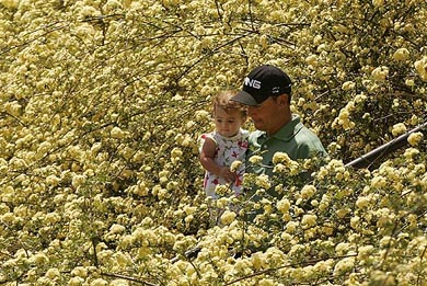 Golfer Chris DiMarco carries his one-year-old daughter as he makes his way down a staircase to the eighth green surrounded by blooming bushes during the Masters par-three tournament in Augusta, Georgia, on Thursday