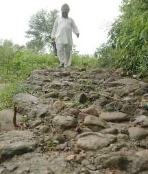 A villager trudges on a damaged footpath in Baloli village.