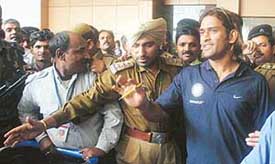 Security personnel try to give cover to Mahendra Singh Dhoni at the Indira Gandhi International Airport in New Delhi on Monday after Team India arrived from the tour of Pakistan. 