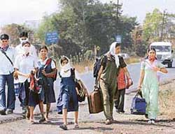 Students cover their noses as they walk along with villagers towards the state transport bus stand with their belongings to leave their villages as they fear contamination by the deadly bird flu virus outside Navapur in Nandurbar district of western Maharashtra on Thursday.