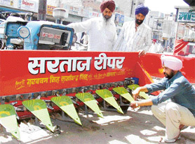 Two farmers from Manikpur village of Rajasthan watch Sukhwinder Singh fit a reaper onto a tractor at Mansa.