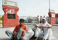 A woman, along with her grandson, waits for a bus in front of the closed main gate of the bus stand in Patiala