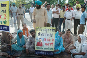 Members of the Mritak Mulazim Ashrit Sangharsh Committee block the main gate of the PSEB headquarters in Patiala on Wednesday.