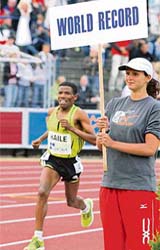 Haile Gebrselassie of Ethiopia runs past a board marking the old world record in the one-hour running event