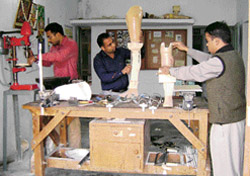 A prosthetic engineer and two technicians prepare artificial limbs and a caliper at the workshop of the DDRC in Sangrur