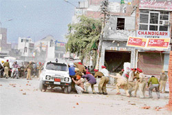 Policemen take shelter behind the official vehicle of the SDM as agitators pelt stones on government officials in Amritsar