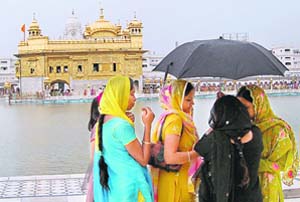 Devotees huddle under an umbrella during rain in Amritsar on Tuesday.