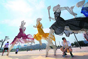 A student sits in the shade of Olympic statues in front of the National Stadium known as the Bird's Nest.