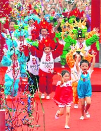 Children dressed in Olympic costumes run onto the stage during the official opening ceremony for the Olympic village